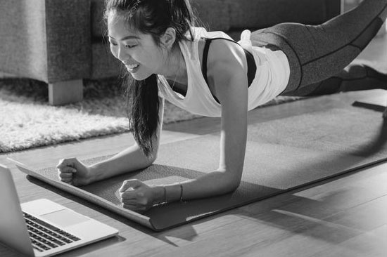 Een vrouw van middelbare leeftijd die thuis voor haar laptop een plank uitoefent .