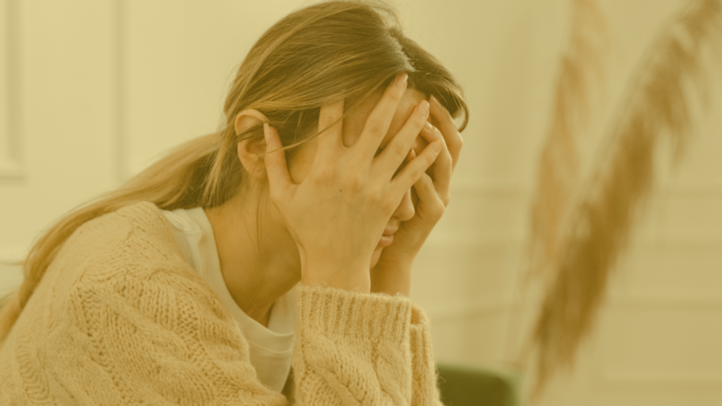 Een vrouw die met haar handen in haar haar zit doordat ze stress ervaart.