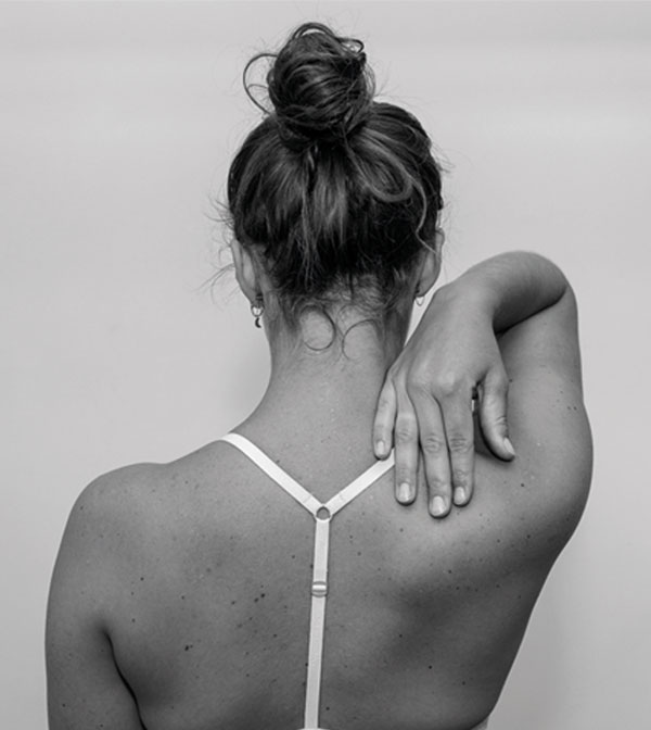 Fysiotherapie: ieder mens en lichaam is uniek De rug en het achterhoofd van een vrouw met een sport-bh de vrouw raakt met haar hand haar schouder aan.